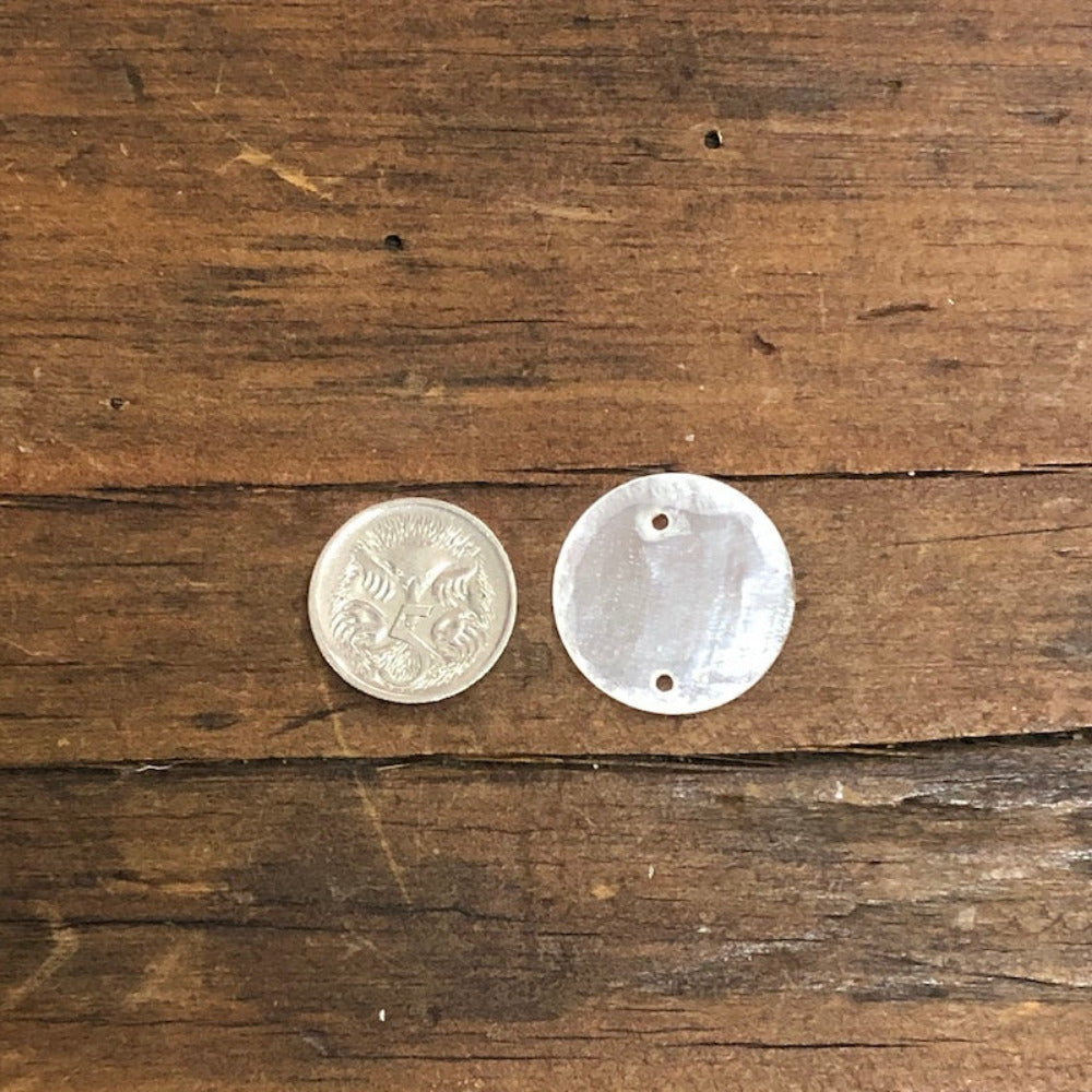 oyster shell disc with two pre drilled holes to use for making hanging decorations or craft projects on a wooden surface