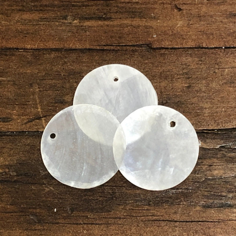 oyster shell disc with one pre drilled holesto use for making hanging decorations or craft projects on a wooden surface