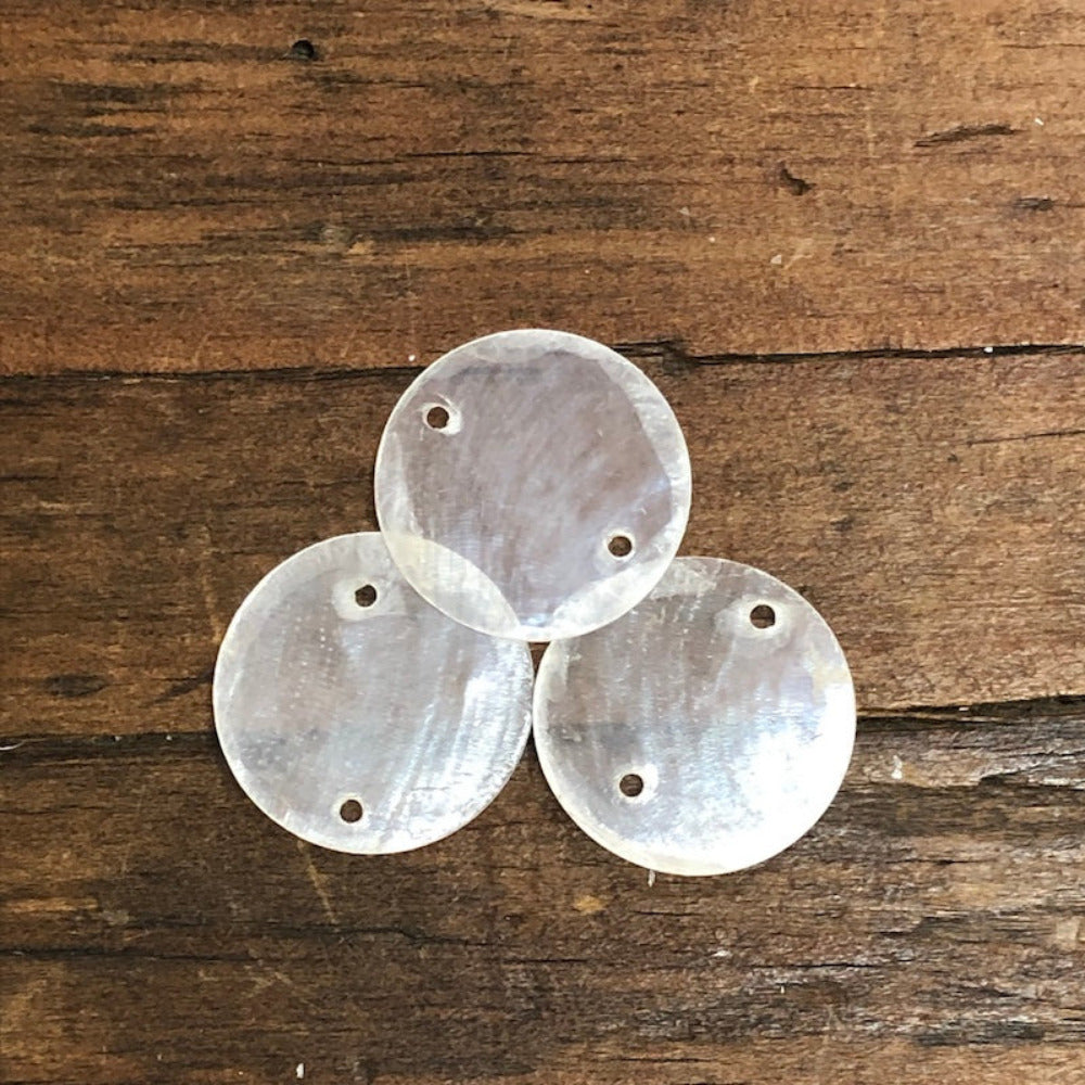 oyster shell disc with two pre drilled holes to use for making hanging decorations or craft projects on a wooden surface