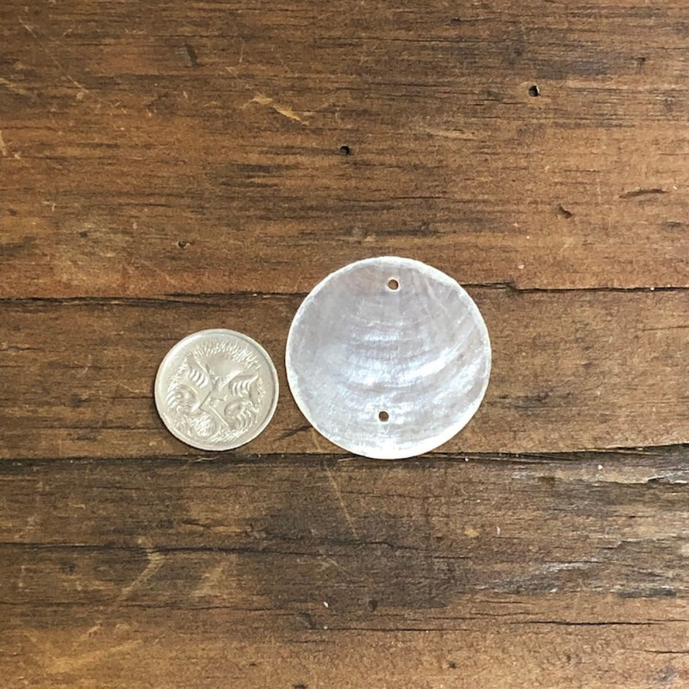 oyster shell disc with two pre drilled holes to use for making hanging decorations or craft projects on a wooden surface