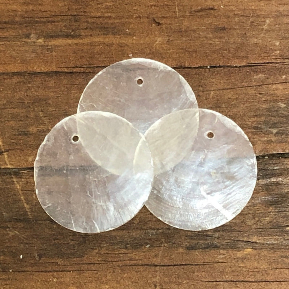 oyster shell disc with one pre drilled hole to use for making hanging decorations or craft projects on a wooden surface
