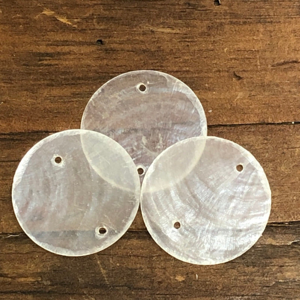 oyster shell disc with two pre drilled holes to use for making hanging decorations or craft projects on a wooden surface