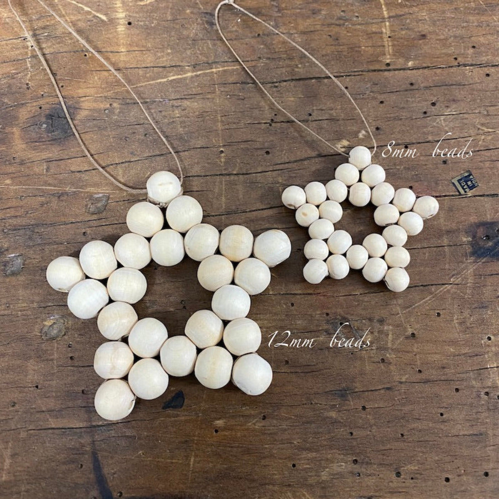 Two decorative stars with raw wood beads and camel-colored flat waxed cord woven together displayed on a wood surface