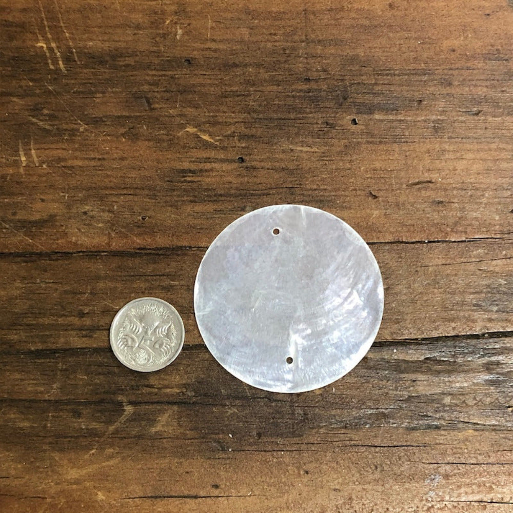 oyster shell disc with two pre drilled holes to use for making hanging decorations or craft projects on a wooden surface