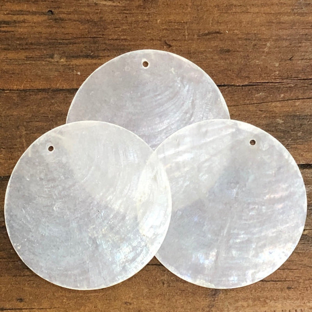 oyster shell disc with one pre drilled holes to use for making hanging decorations or craft projects on a wooden surface