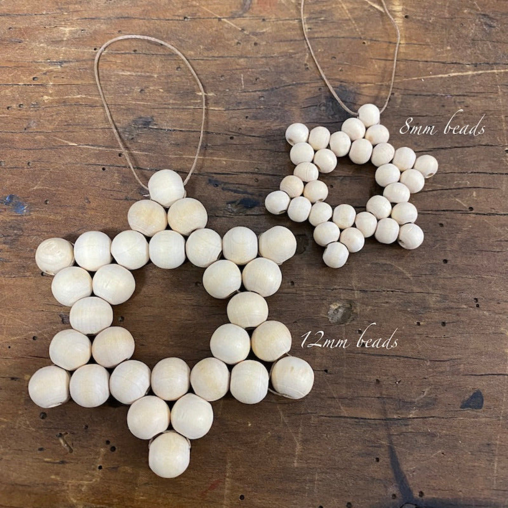 Two decorative stars with raw wood beads and camel-colored flat waxed cord woven together displayed on a wood surface