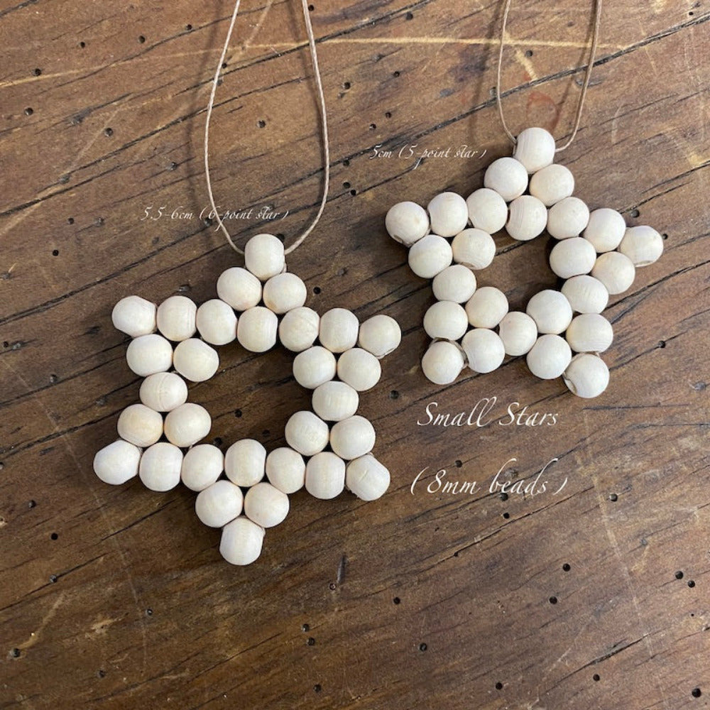 Two decorative stars with raw wood beads and camel-colored flat waxed cord woven together displayed on a wood surface
