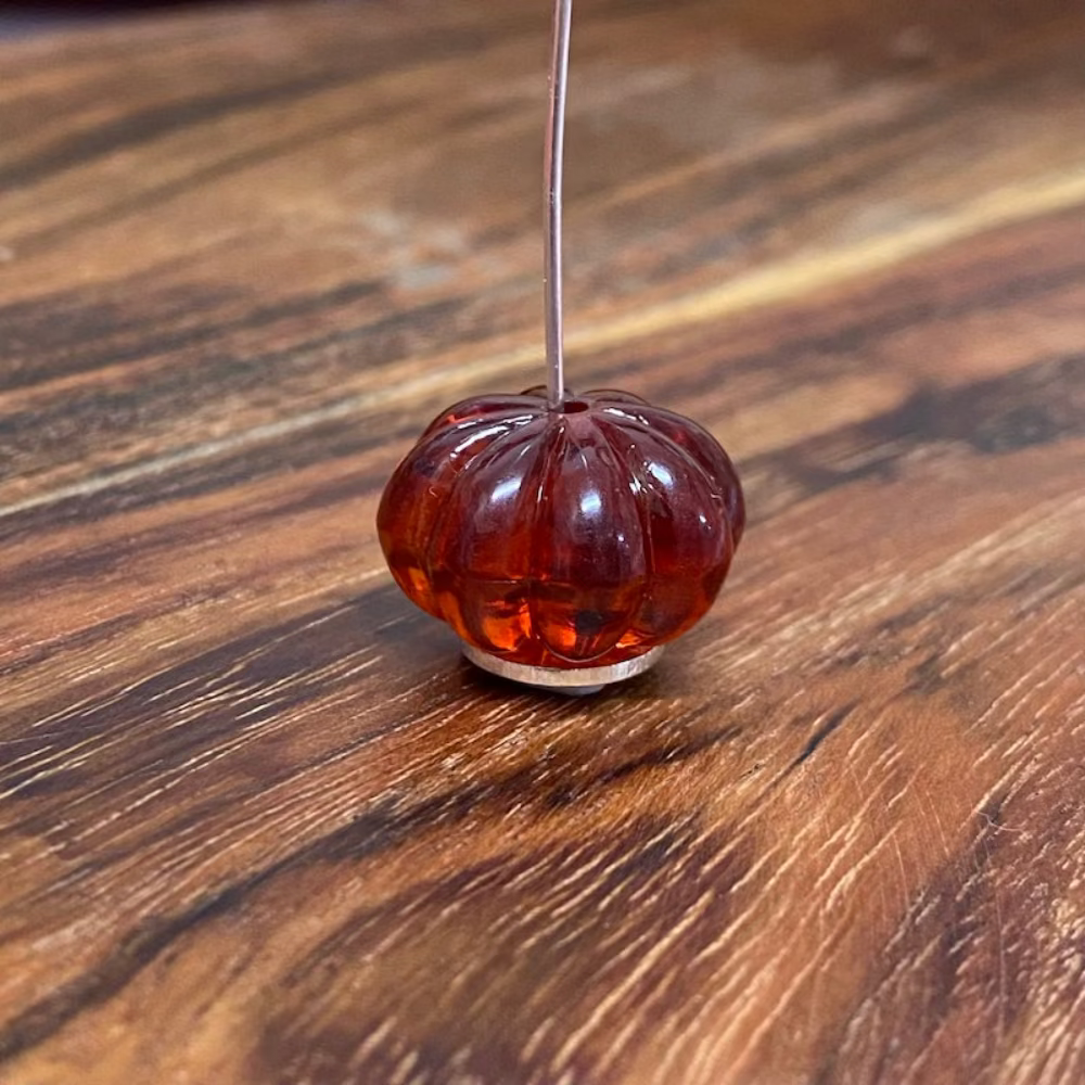 One transparent amber pumpkin shape beads with black markings, displayed on a wooden surface