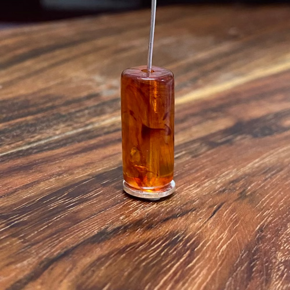 one tube bead on a pin with a wood background in amber colour