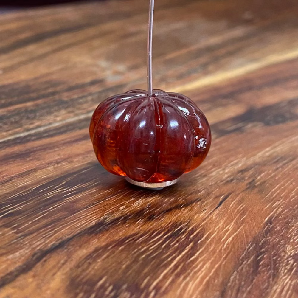 One transparent amber pumpkin shape beads with black markings, displayed on a wooden surface