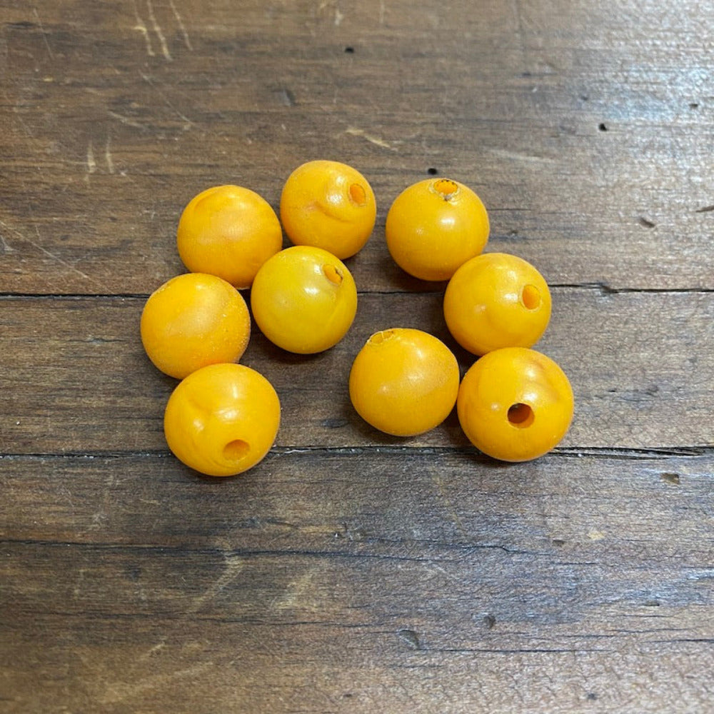 A collection of vintage phenolic amber beads in a buttery yellow colour showing large visible holes for the purpose of jewelry making and craft on a wood surface