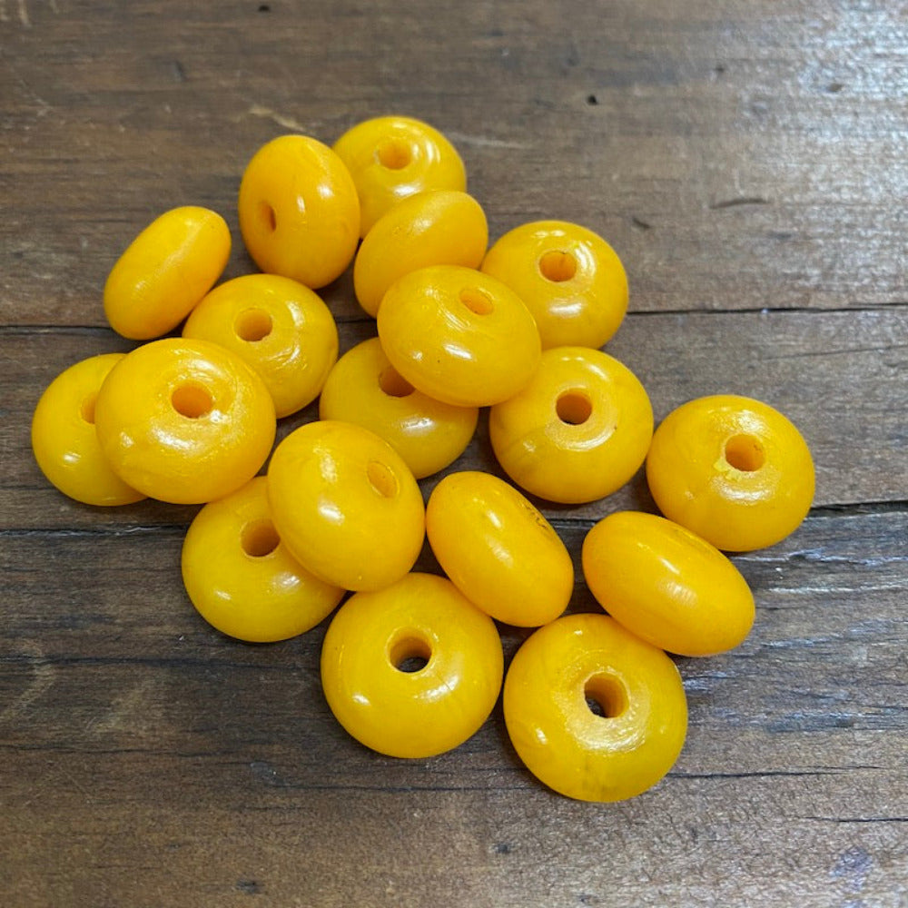 A collection of vintage phenolic amber beads in a buttery yellow colour showing large visible holes for the purpose of jewelry making and craft on a wood surface