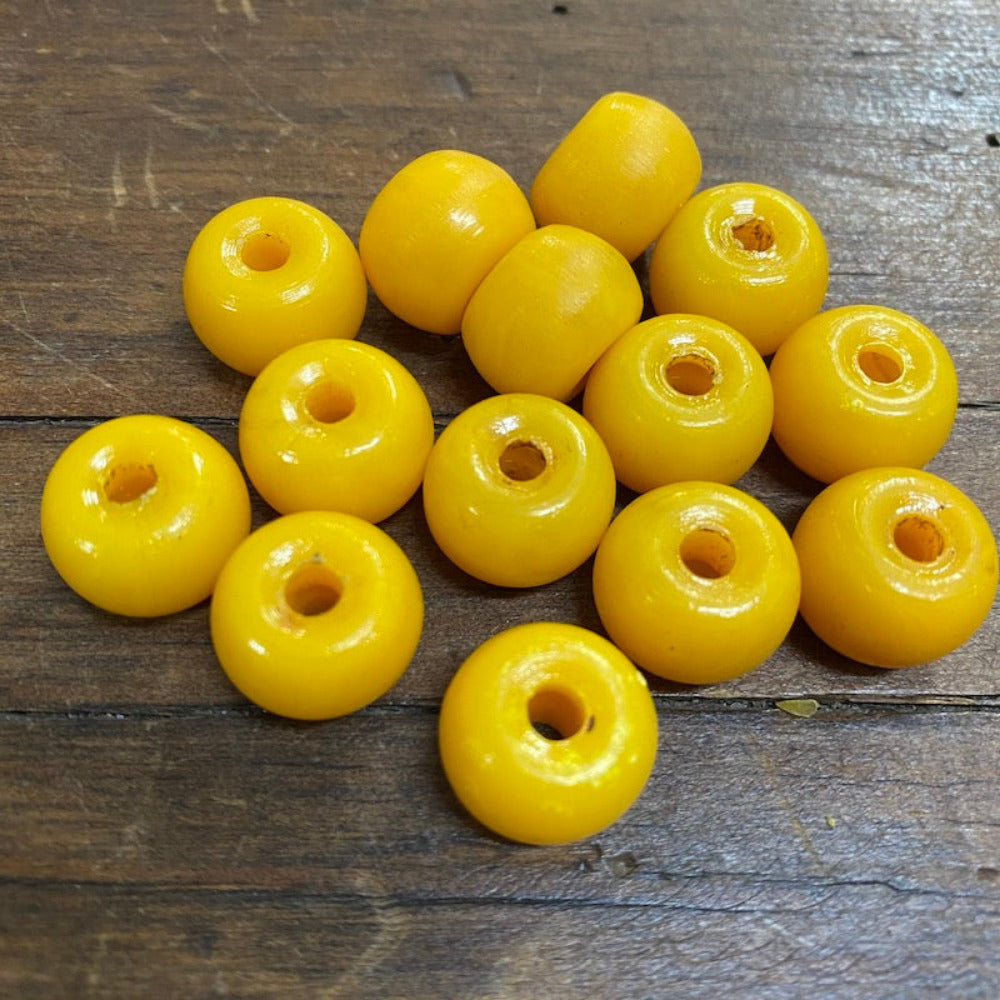 A collection of vintage phenolic amber beads in a buttery yellow colour showing large visible holes for the purpose of jewelry making and craft on a wood surface