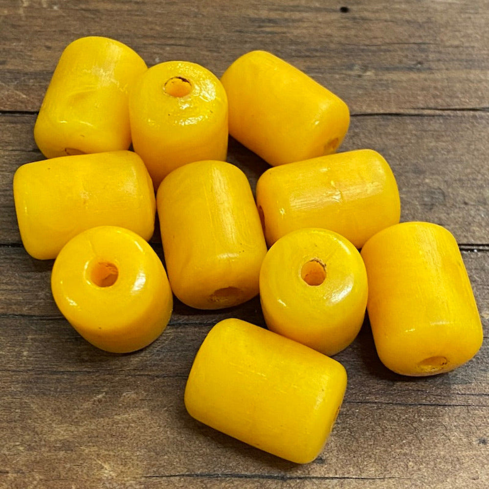 A collection of vintage phenolic amber beads in a buttery yellow colour showing large visible holes for the purpose of jewelry making and craft on a wood surface