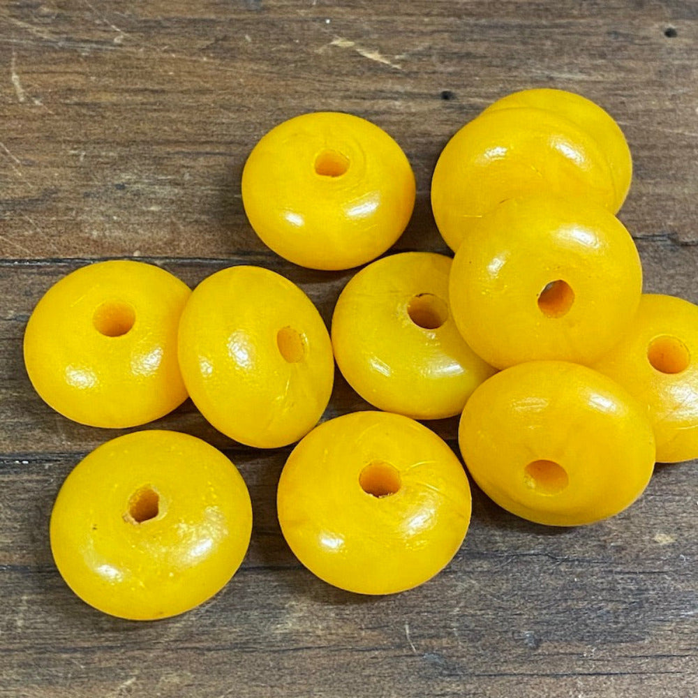 A collection of vintage phenolic amber beads in a buttery yellow colour showing large visible holes for the purpose of jewelry making and craft on a wood background