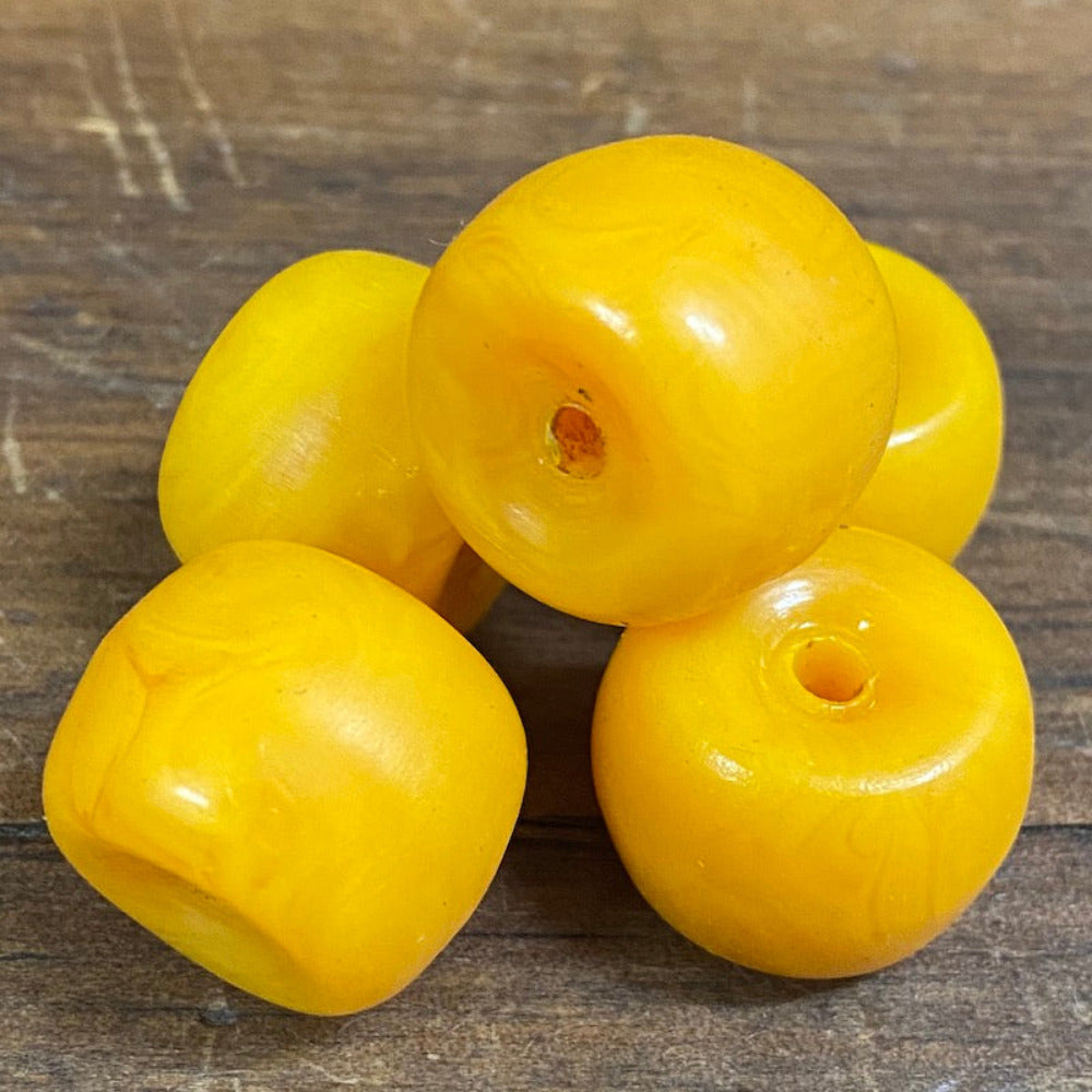 A collection of vintage phenolic amber beads in a buttery yellow colour showing large visible holes for the purpose of jewelry making and craft on a wood surface