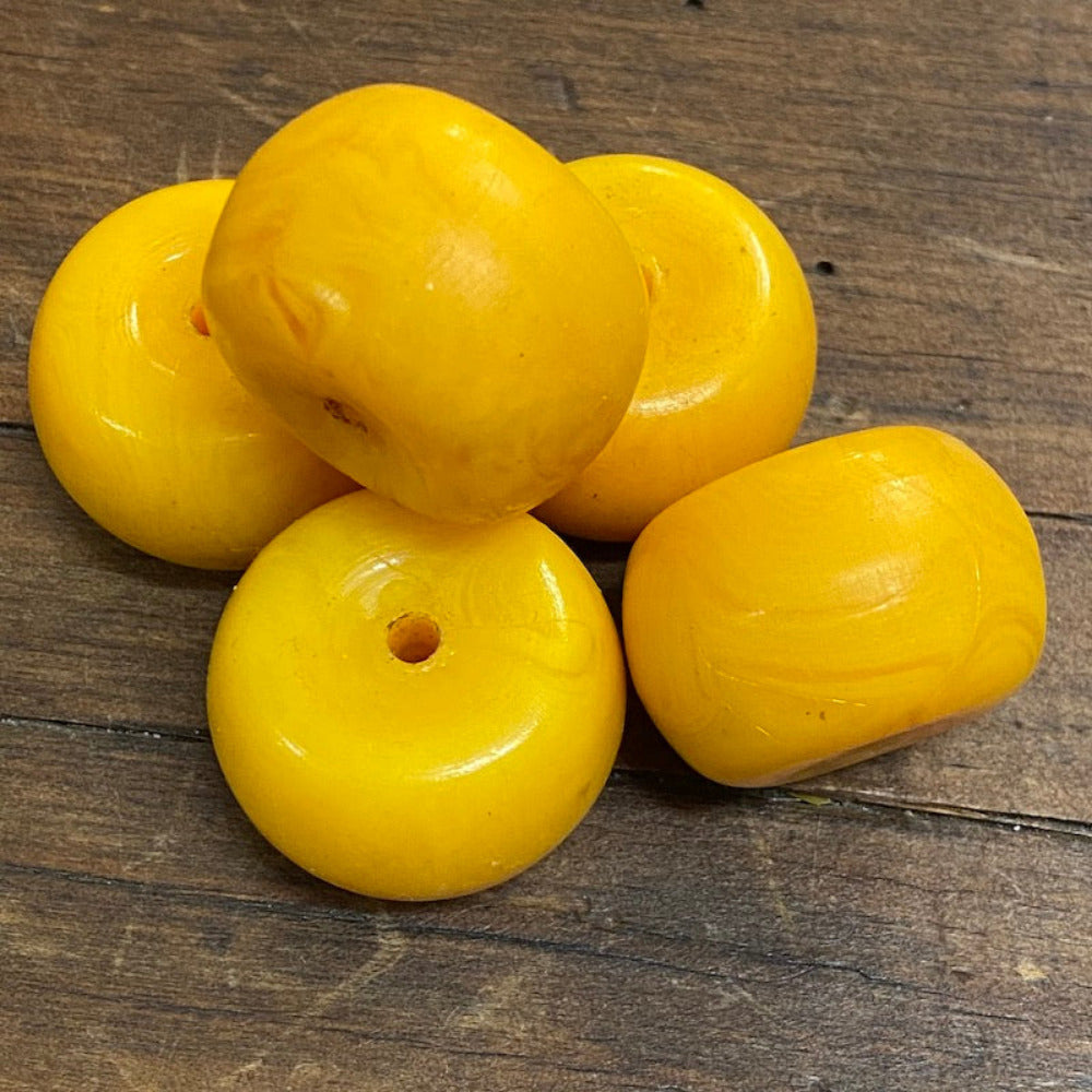 A collection of vintage phenolic amber beads in a buttery yellow colour showing large visible holes for the purpose of jewelry making and craft on a wood surface