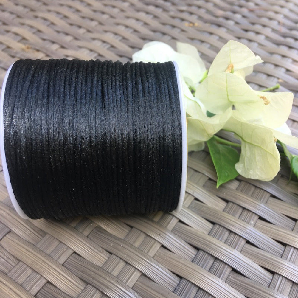 A spool of rat tail cord used for crafting, displayed alongside some white flowers and green leaves on a wicker surface