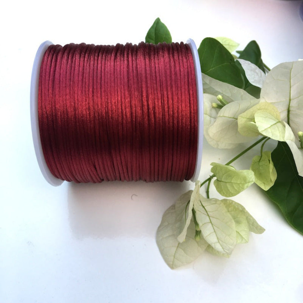 A spool of red rat tail cord used for crafting, displayed alongside some decorative leaves.