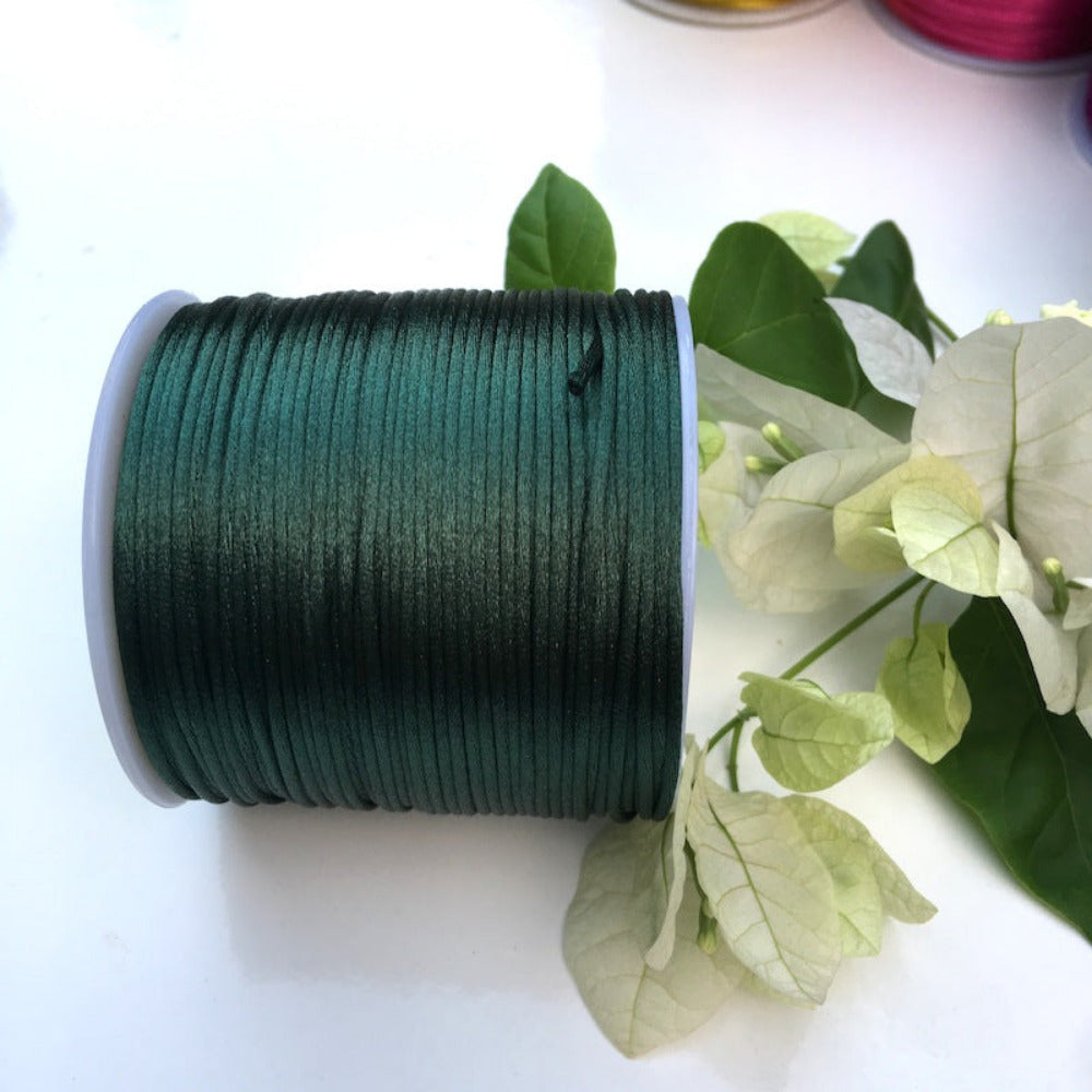 A spool of dark green rat tail cord used for crafting, displayed alongside some leaves.