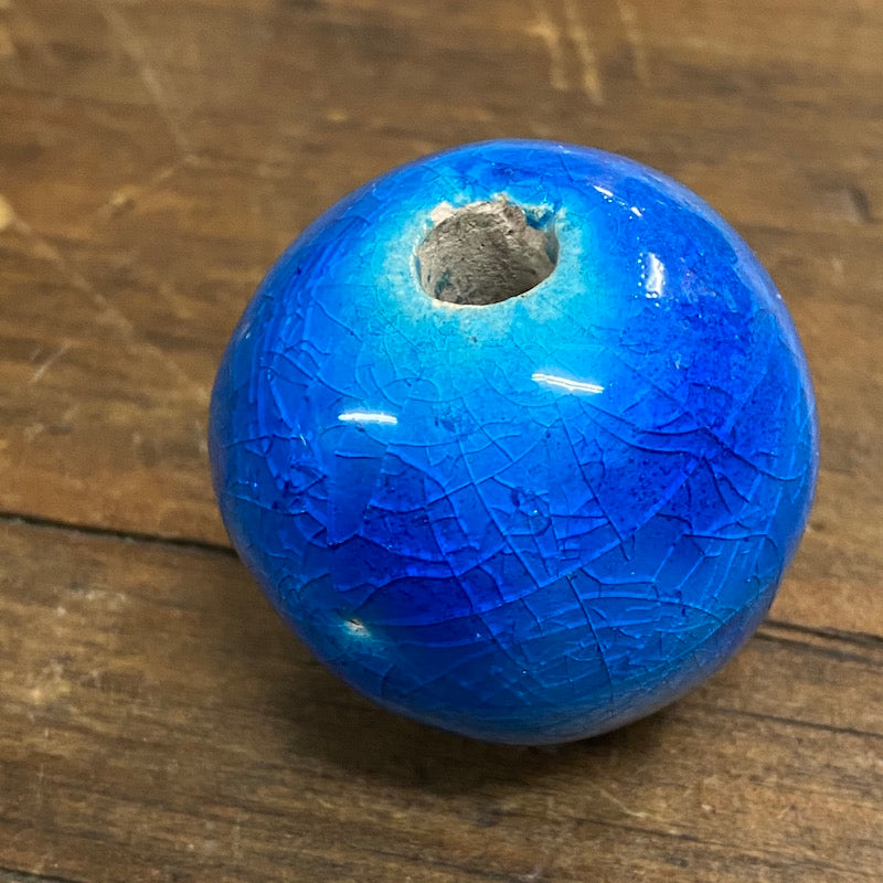 A large, round, cobalt blue ceramic bead with a visible hole in the center for threading, placed on a wooden surface.