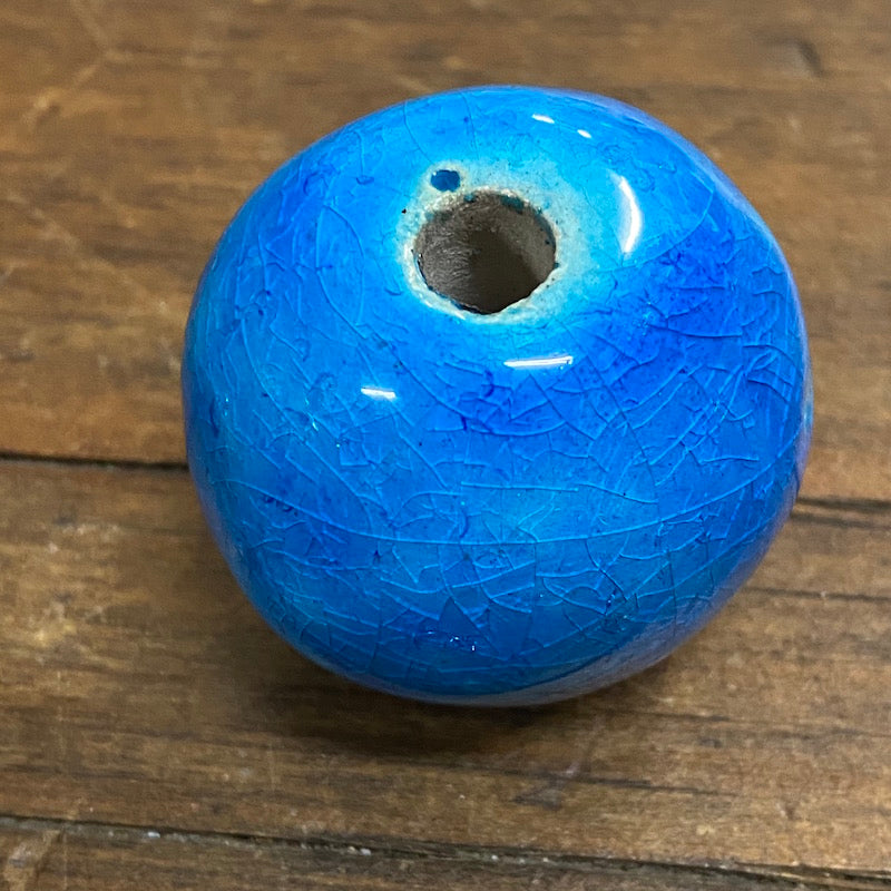 One round, cobalt blue vintage glazed ceramic beads with a visible hole in the center for threading, placed on a wooden surface.