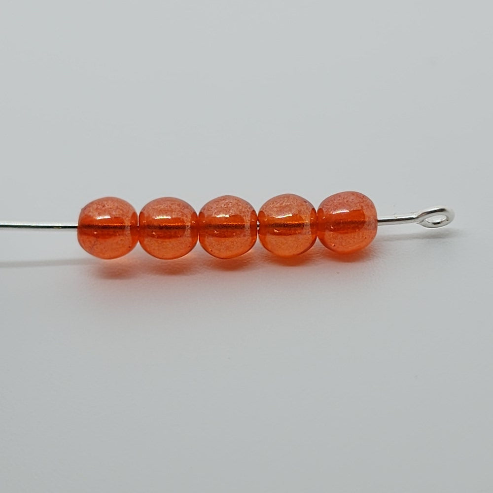 A collection of orange round Czech glass beads on a white surface threaded on a pin