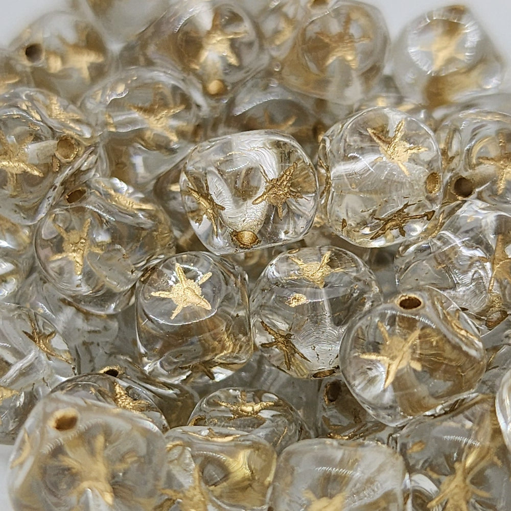 A collection of clear cube-shaped beads with gold etched stars, intended for use in jewelry making.