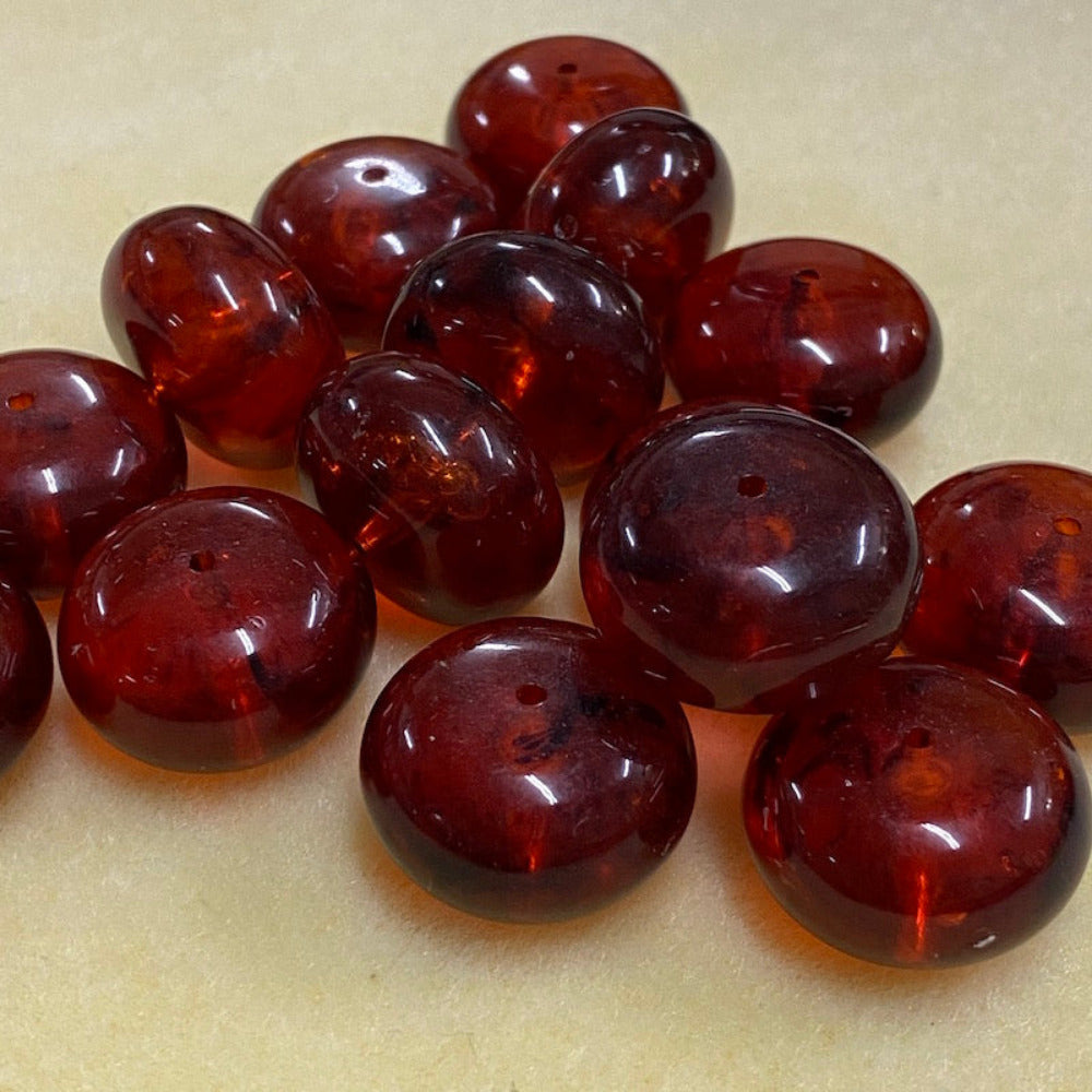 A close-up image of round red amber-colored beads with black markings, showcasing their glossy finish and hole for stringing on a cream background