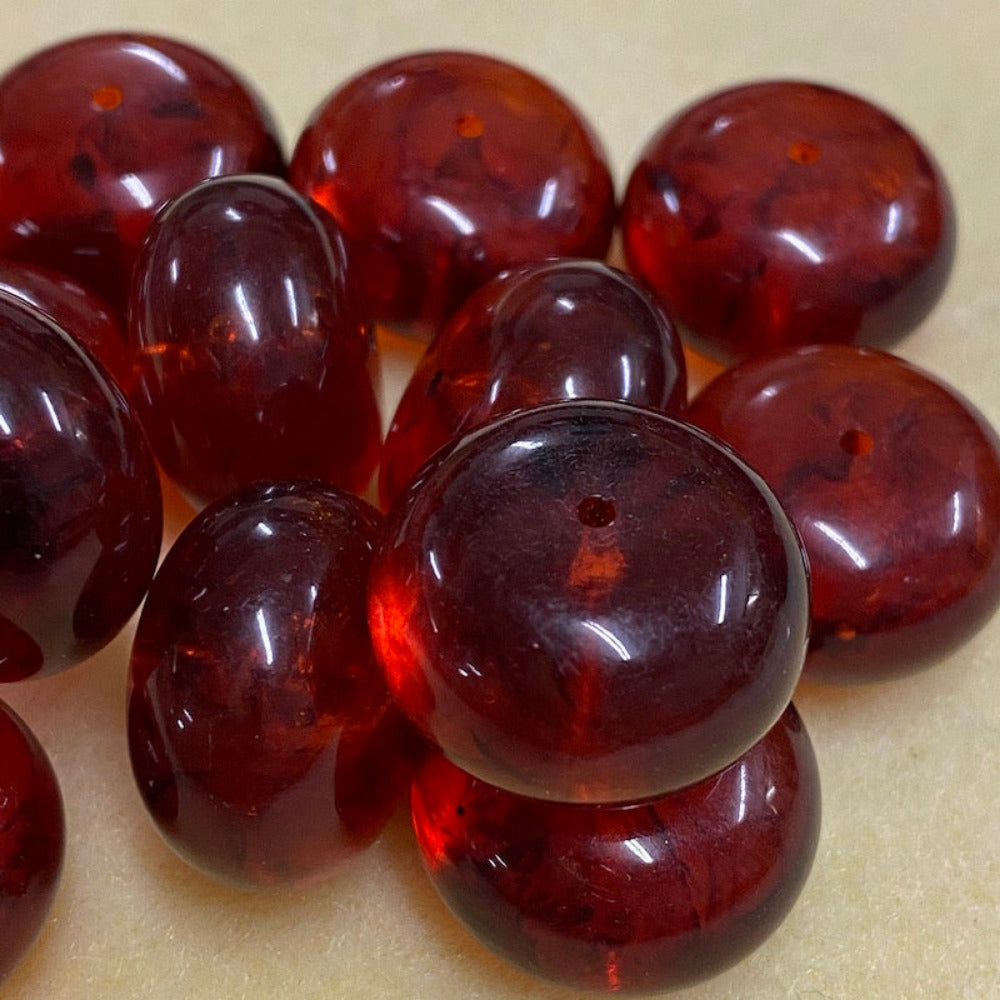 A close-up image of round red amber-colored beads with black markings, showcasing their glossy finish and hole for stringing on a cream background