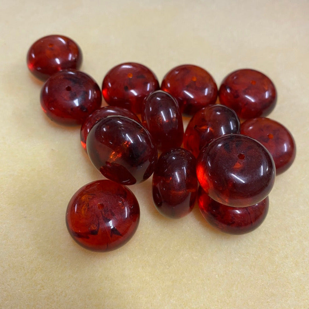 A close-up image of round red amber-colored beads with black markings, showcasing their glossy finish and hole for stringing on a cream background