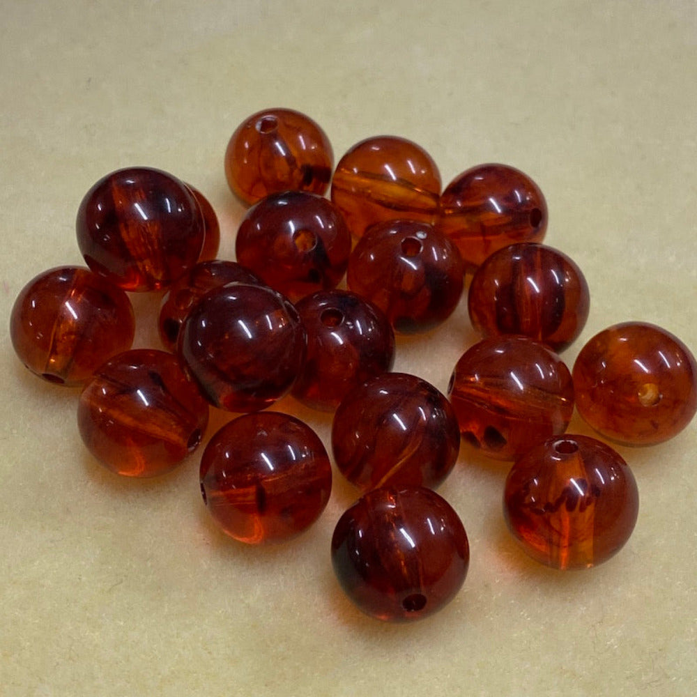 a group of round transparent amber colour beads displayed on a cream surface with visible holes for stringing jewelry and creating craft
