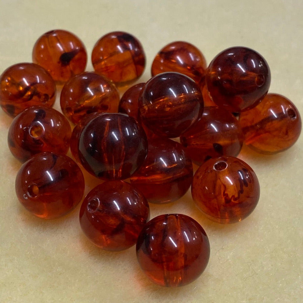 a group of round transparent amber colour beads displayed on a cream surface with visible holes for stringing jewelry and creating craft