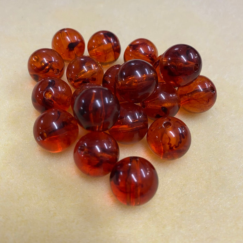 a group of round transparent amber colour beads with black flecks displayed on a cream surface with visible holes for stringing jewelry and creating craft