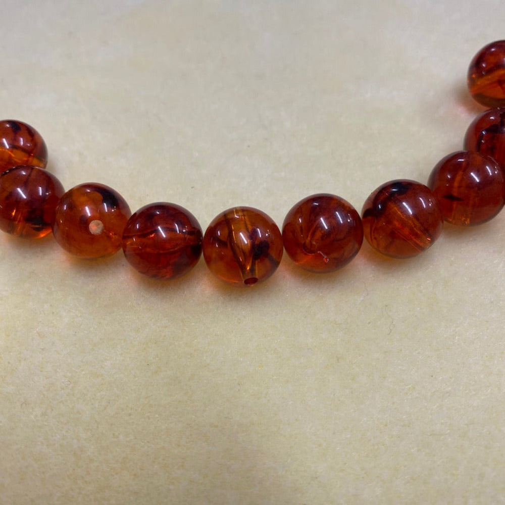 a group of round transparent amber colour beads displayed on a cream surface with visible holes for stringing jewelry and creating craft
