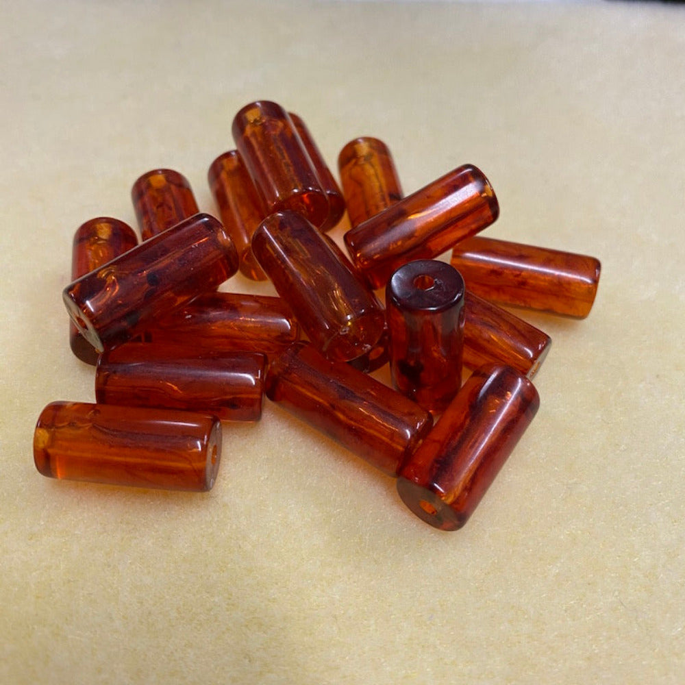 a group of tube shaped amber beads showing the threading hole for the purpose of making jewelry on a cream background