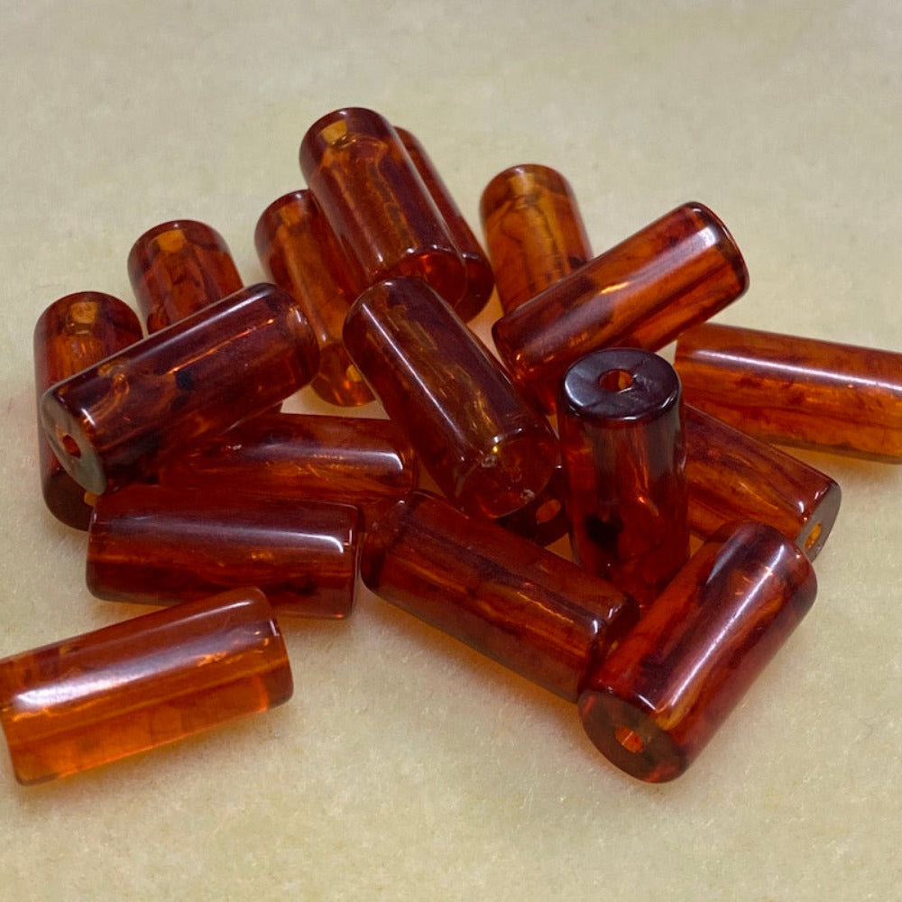 a group of tube shaped amber beads showing the threading hole for the purpose of making jewelry on a cream background