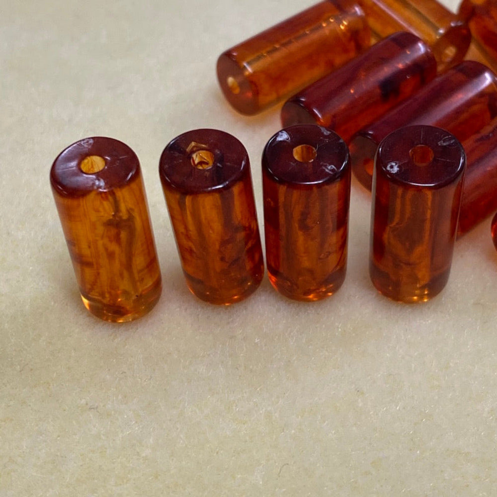 four tube shaped amber beads standing upright to show the threading hole for the purpose of making jewelry on a cream background