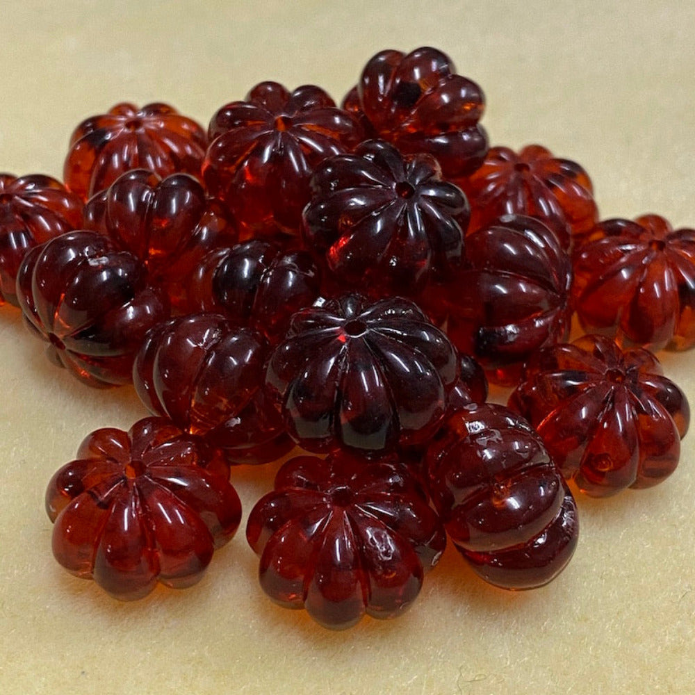 a collection of transparent amber pumpkin shape beads with black markings, displayed on a cream surface