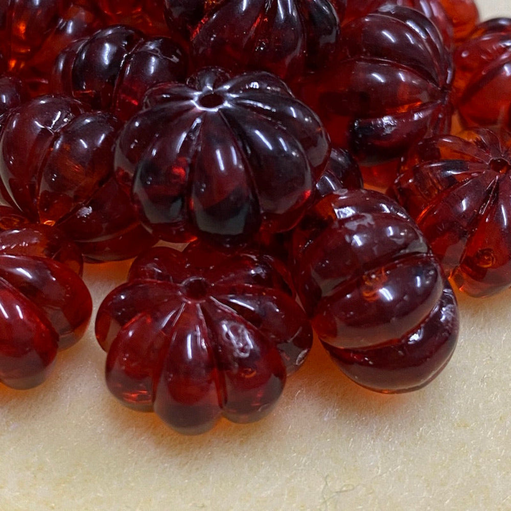 a collection of transparent amber pumpkin shape beads with black markings, displayed on a cream surface