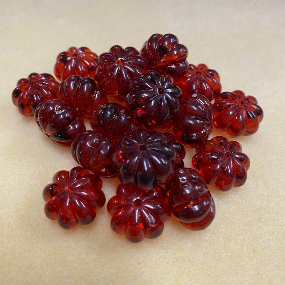 a collection of transparent amber pumpkin shape beads with black markings, displayed on a cream surface