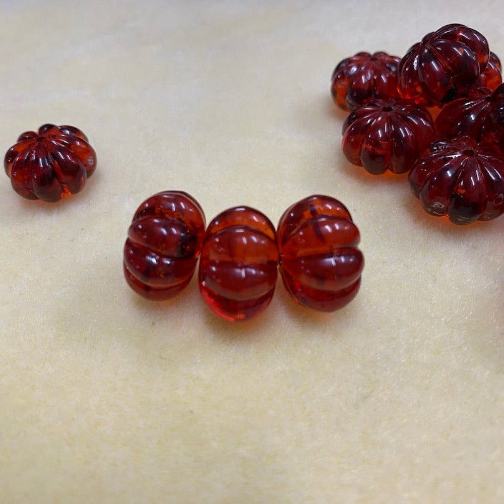 a collection transparent amber pumpkin shape beads with black markings, displayed on a cream surface