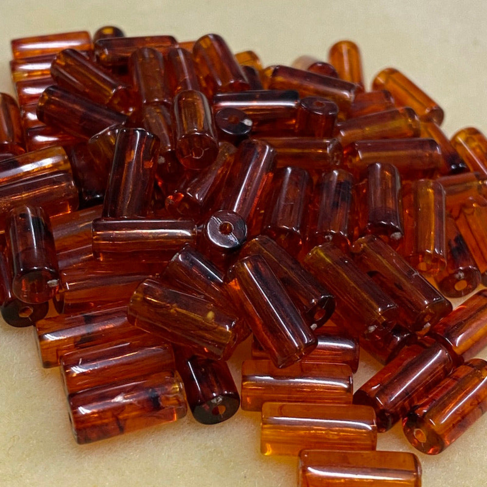 a group of transparent amber colour tube shape beads displayed on a cream surface with visible holes for stringing jewelry and creating craft