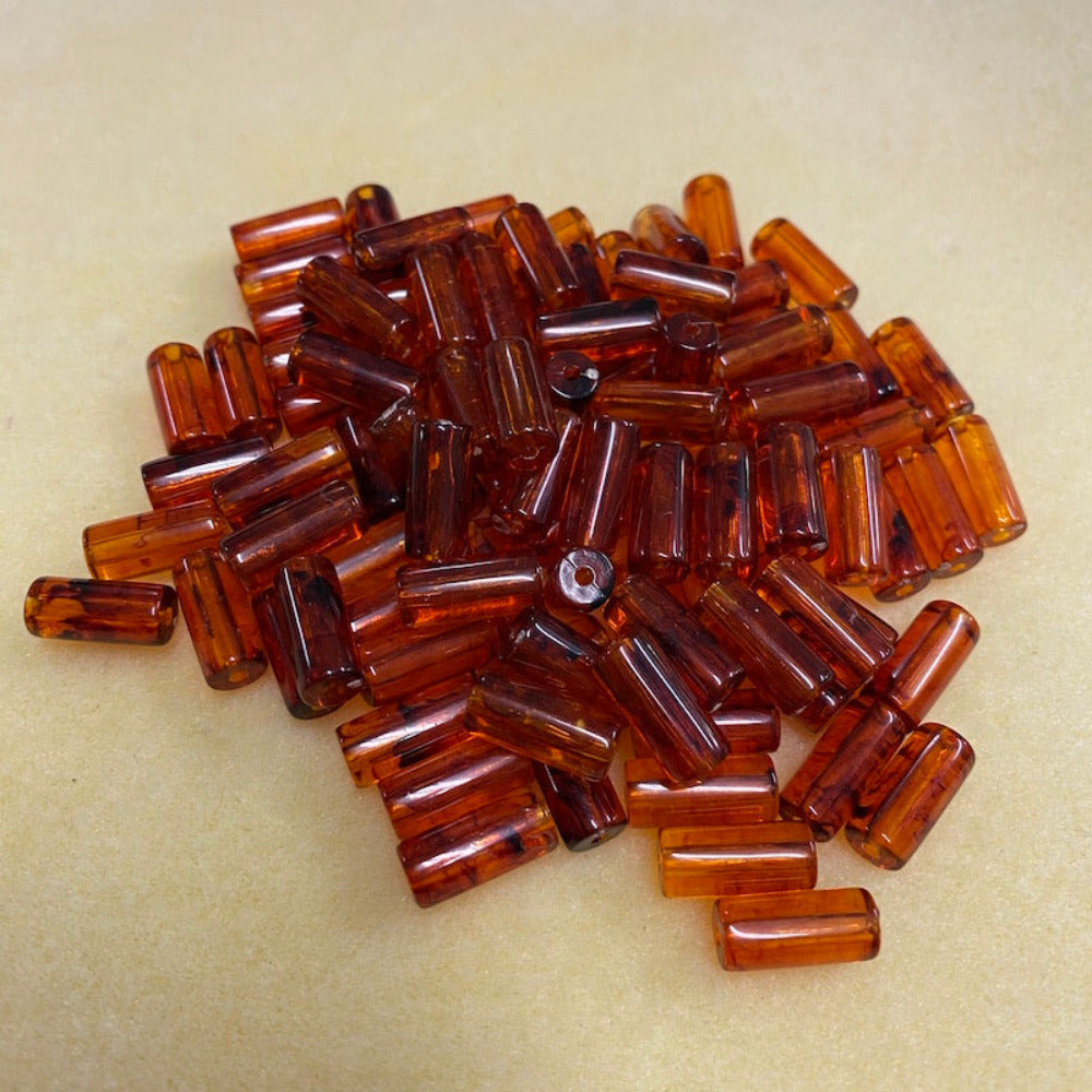 a group of transparent amber colour tube shape beads displayed on a cream surface with visible holes for stringing jewelry and creating craft