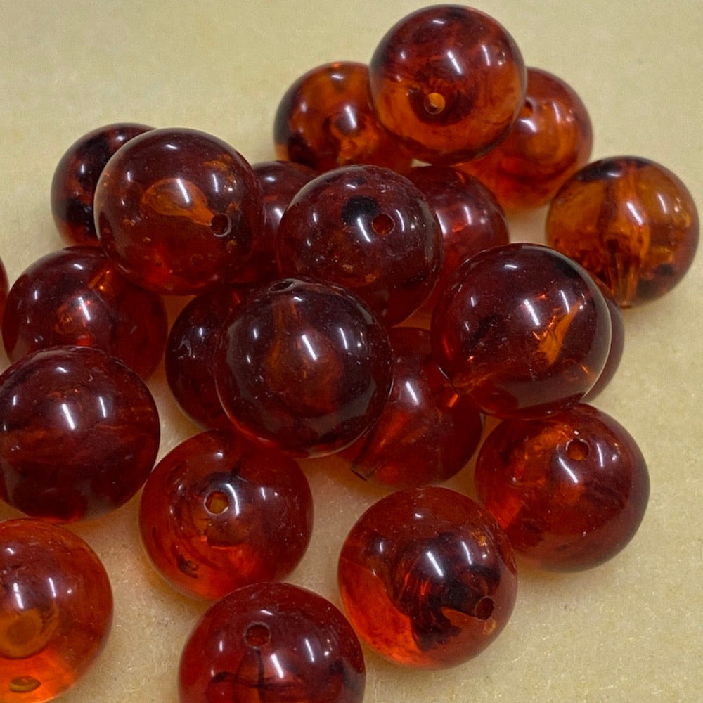 a group of round transparent amber colour beads displayed on a cream surface with visible holes for stringing jewelry and creating craft