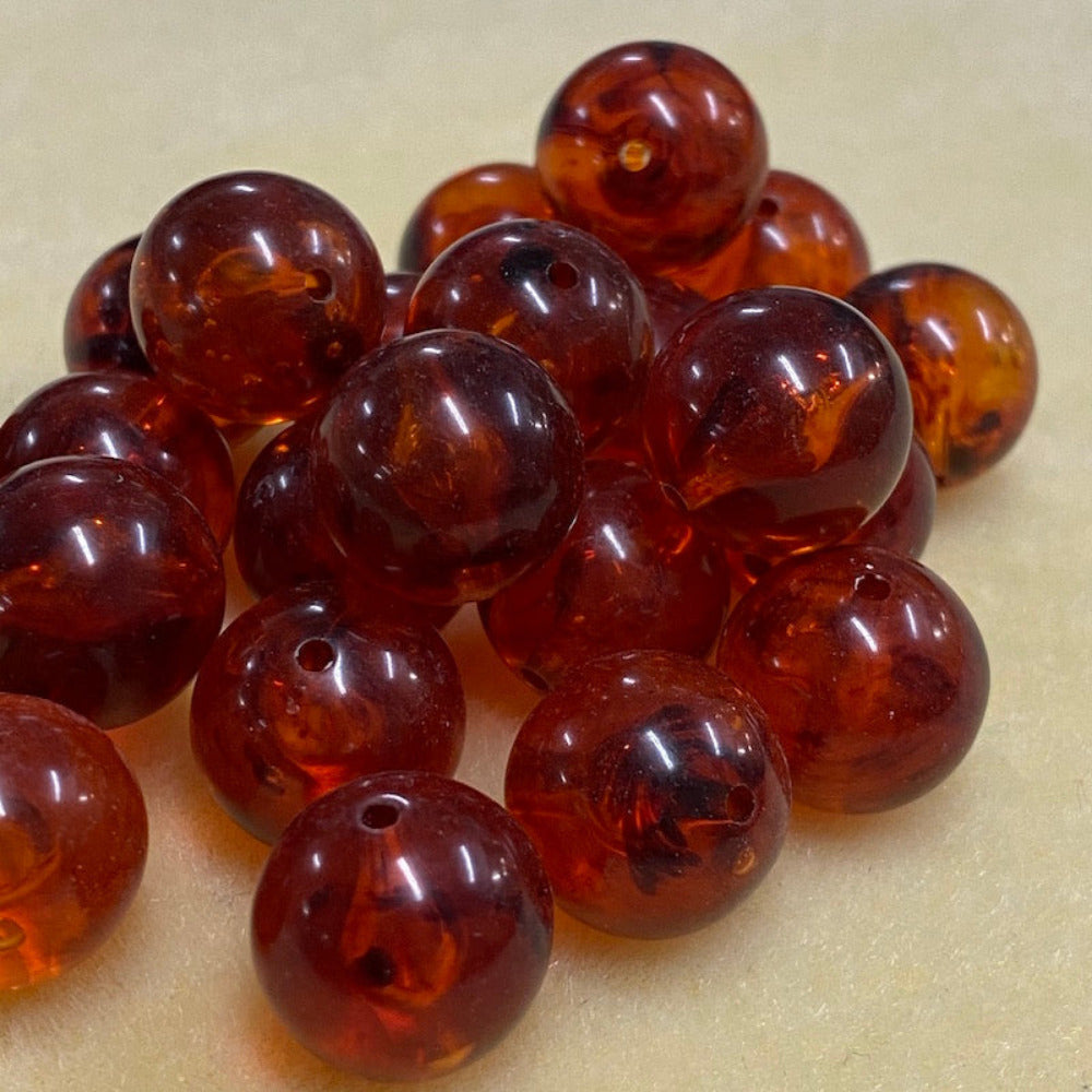 a group of round transparent amber colour beads displayed on a cream surface with visible holes for stringing jewelry and creating craft