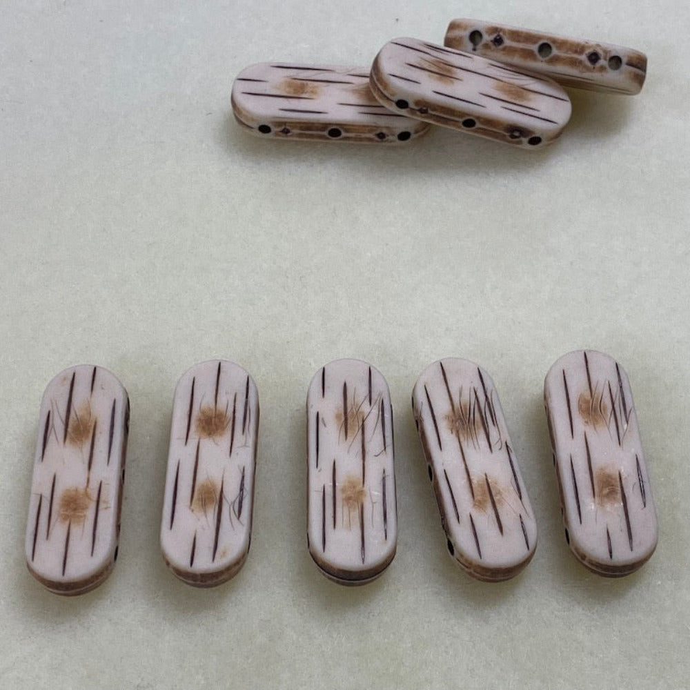bone look flat beads with 3 threading holes on a cream surface in a line and with 3 in a pile showing the holes