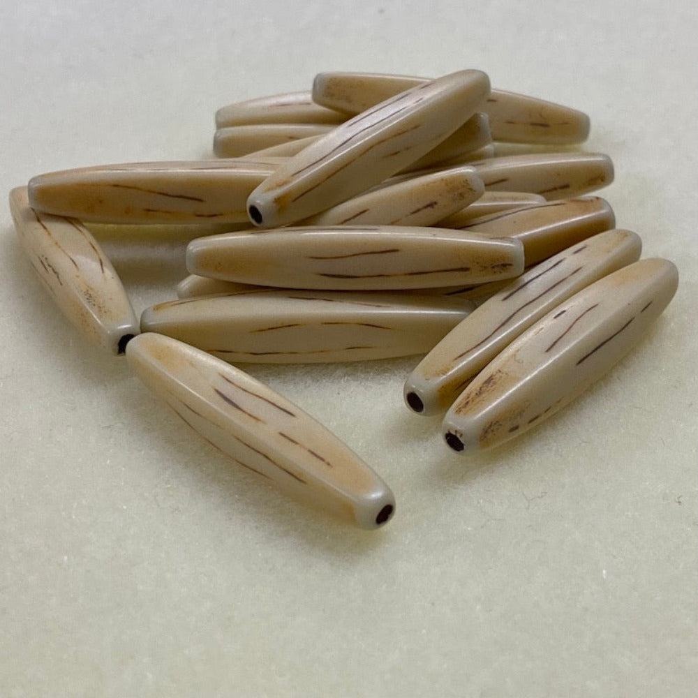 A collection of light brown, bone-shaped beads with a threading hole on, arranged in a line on a beige background.