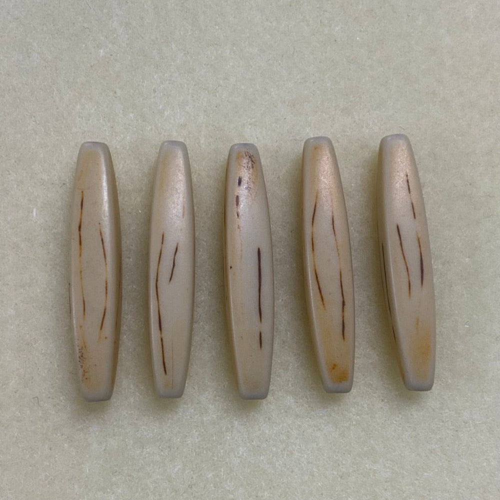 A collection of light brown, hair pipe shaped beads with a threading hole arranged in a line on a beige background.