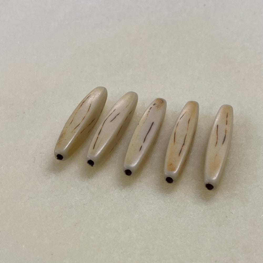 A collection of light brown, hair pipe shaped beads with a threading hole arranged in a line on a beige background for the use of jewelry or tribal embellishment making